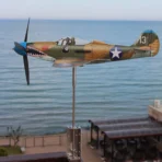 Stainless steel Bell P39 Airacobra aircraft weathervane and wind spinner installed on balcony rail against the sea