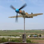 Stainless steel P39 fighter weathervane model demonstrates living kinetic art on terrace against countryside environment