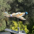 Steel P39 fighter aircraft model functioning as a wind-driven kinetic sculpture above an olive grove